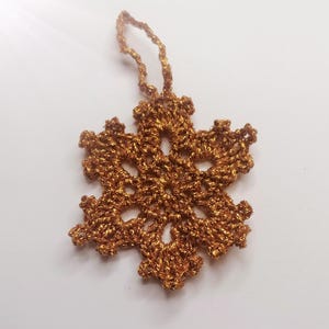 Peut inclure: Ornement en forme de flocon de neige en crochet doré métallique. L'étoile à six branches est dotée d'une boucle de suspension. Le motif complexe est réalisé avec un fil brillant et texturé. Décoration festive pour Noël ou les fêtes d'hiver.