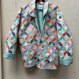 May include: A quilted jacket featuring a colorful patchwork pattern of interlocking circles in shades of red, blue, yellow, and green. The jacket has a notched collar, long sleeves with cuffs, two front patch pockets, and a light green lining.