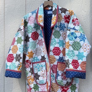 May include: A quilted jacket featuring a patchwork of multicolored star and hexagon patterns in various floral and geometric prints. The garment has a notched collar, two front patch pockets, and blue cuffs with a white cross pattern.