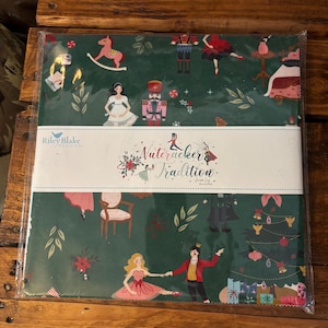 May include: A green fabric panel featuring a Nutcracker-themed design. The design includes illustrations of ballerinas, a nutcracker, a Christmas tree, and the text "Nutcracker Tradition" on a white banner. The Riley Blake Designs logo is visible.