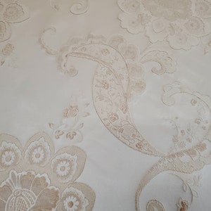 May include: Close-up of a white fabric with a beige floral pattern. The fabric has a raised texture and a delicate design.