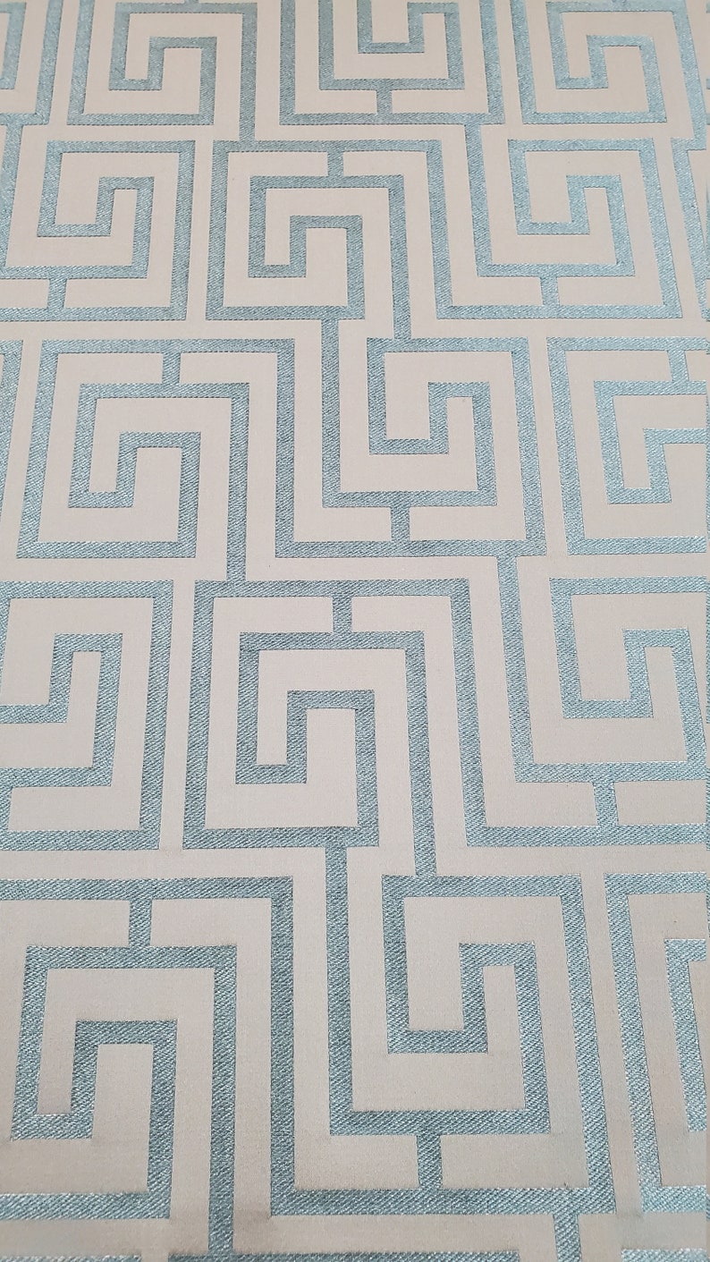 May include: A beige fabric with a repeating pattern of blue interlocking squares. The pattern resembles a maze or a Greek key design.