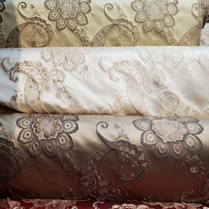 May include: Four rolls of fabric with intricate paisley and floral patterns. The fabric is in shades of beige, brown, and red.