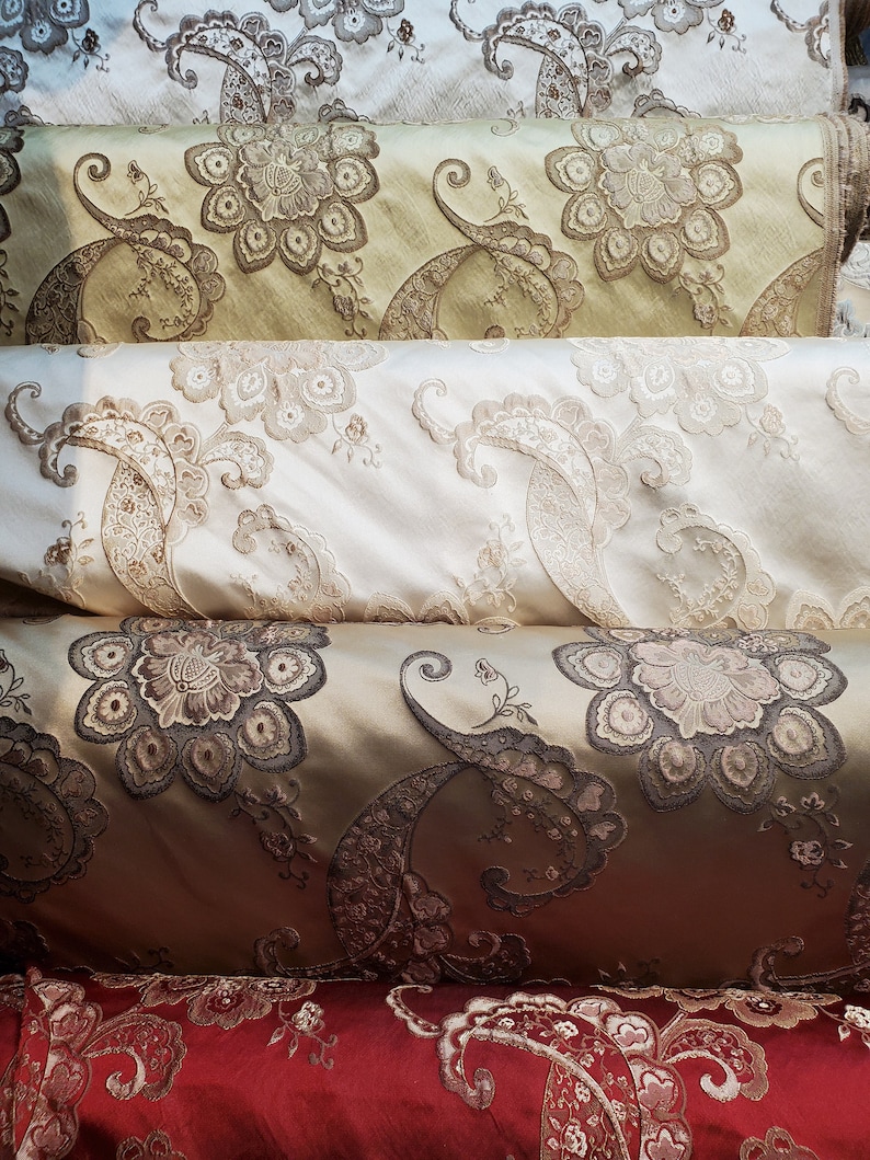 May include: Four rolls of fabric with intricate paisley and floral patterns. The fabric is in shades of beige, brown, and red.