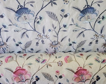 May include: Two rolls of fabric featuring an intricate floral embroidery pattern. The top roll displays blue and tan thread work on a cream background, while the bottom roll showcases vibrant pink and dark blue floral motifs on a light beige fabric.