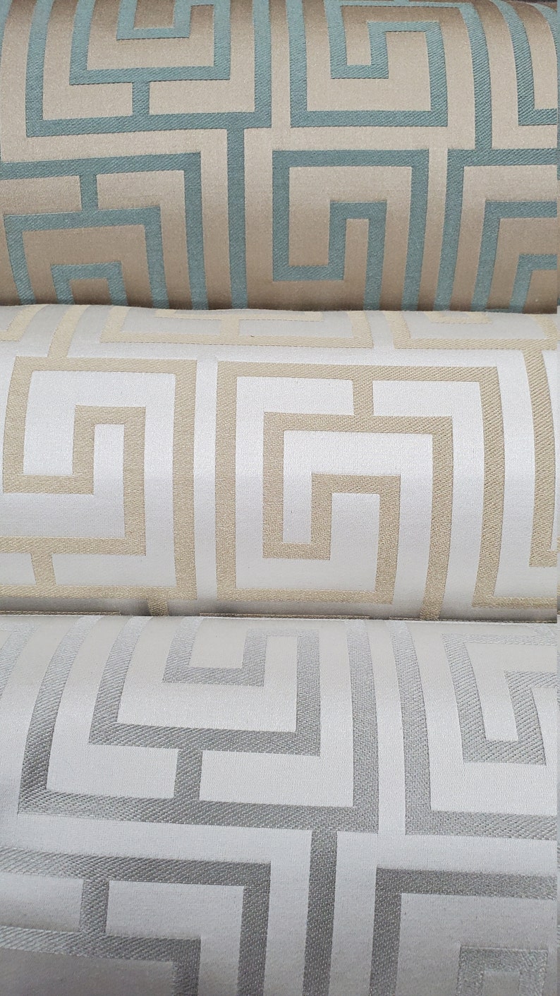 May include: Three fabric samples with a geometric pattern. The top sample is beige with a teal blue pattern. The middle sample is white with a beige pattern. The bottom sample is white with a gray pattern.