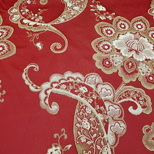 May include: Red fabric with a gold paisley pattern. The fabric has a textured, woven look.