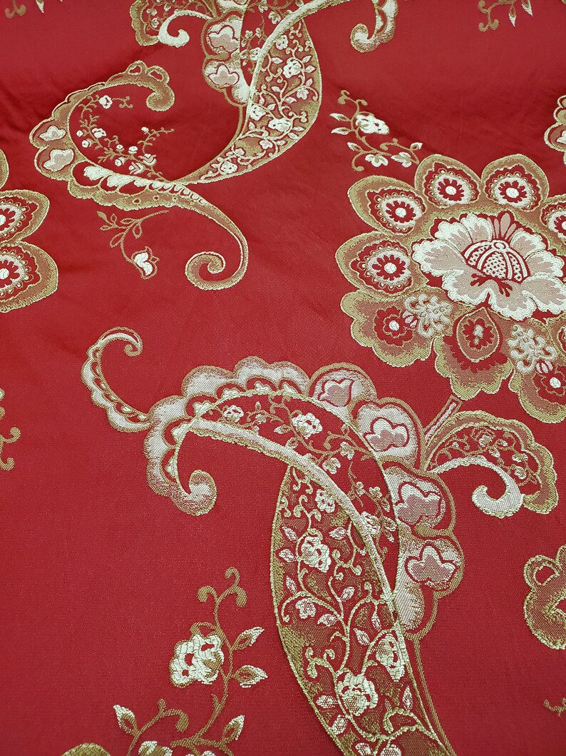 May include: Red fabric with a gold paisley pattern. The fabric has a textured, woven look.