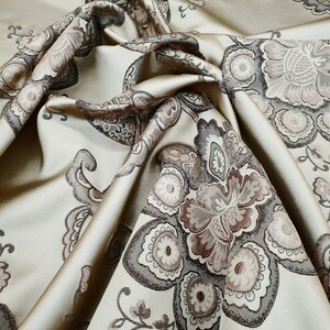 May include: A beige fabric with a brown and gray floral pattern. The fabric is folded and draped, showing the intricate details of the design.