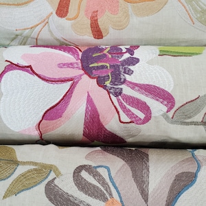 May include: Three embroidered throw pillows with floral designs. The top pillow features a large pink and orange flower, the middle pillow has a large pink and purple flower, and the bottom pillow has a large brown and orange flower.