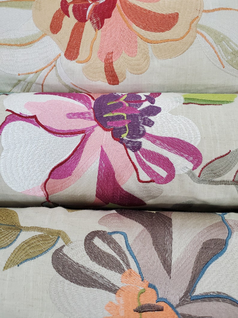 May include: Three embroidered throw pillows with floral designs. The top pillow features a large pink and orange flower, the middle pillow has a large pink and purple flower, and the bottom pillow has a large brown and orange flower.