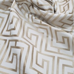 May include: White fabric with a gold geometric pattern of interlocking squares and rectangles.