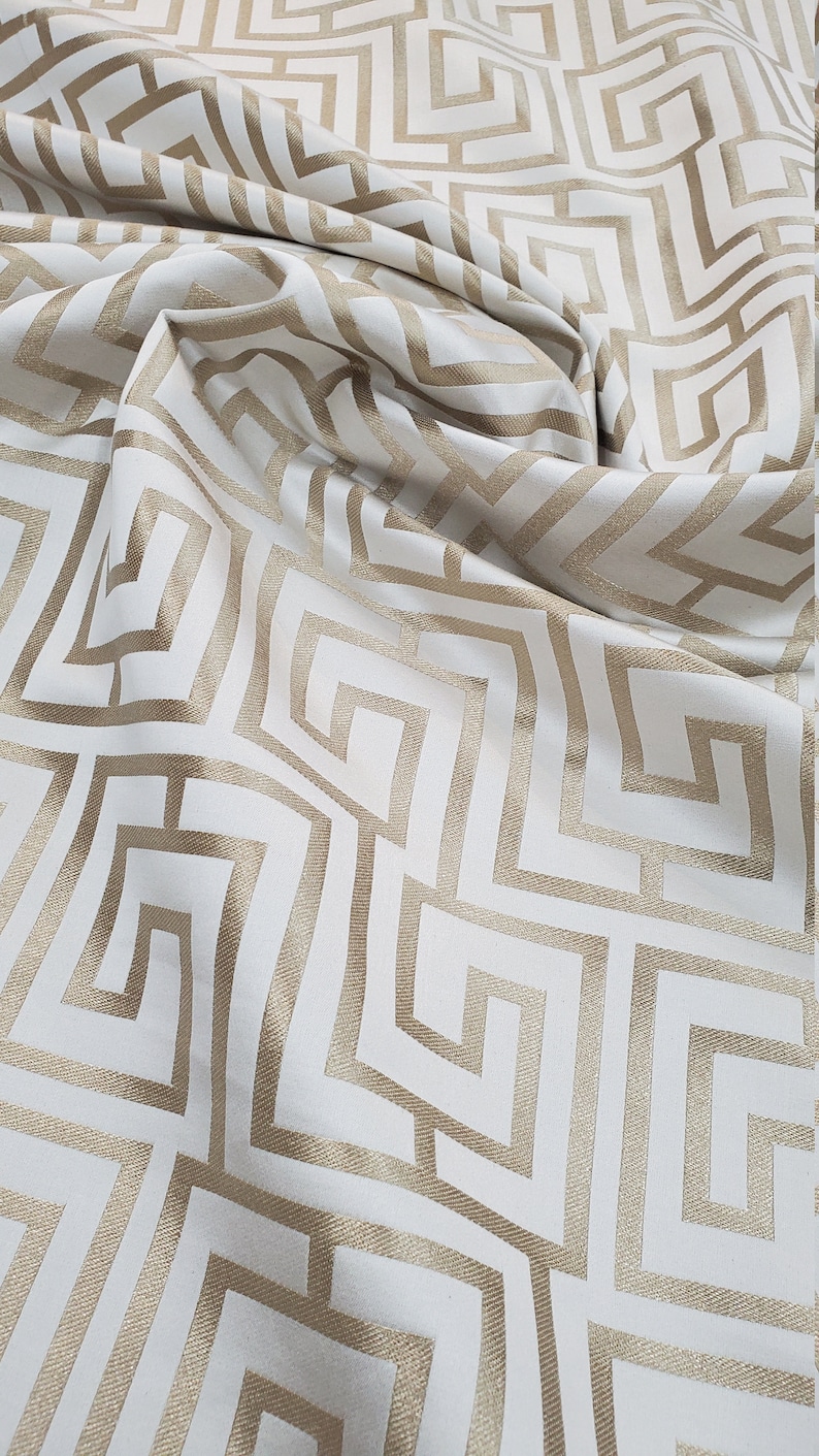 May include: White fabric with a gold geometric pattern of interlocking squares and rectangles.
