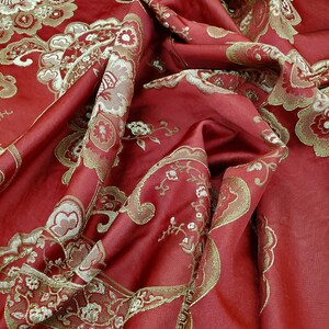 May include: Red fabric with a gold paisley pattern. The fabric is folded and draped, showing the texture and detail of the design.