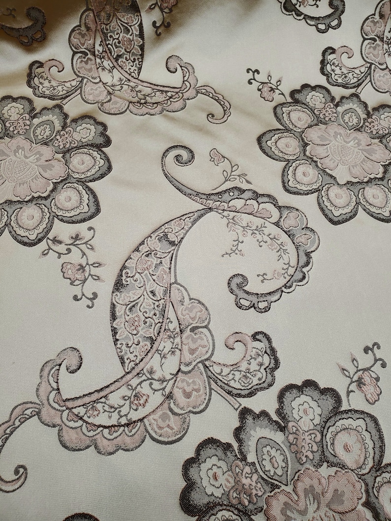 May include: A beige fabric with a paisley pattern in shades of brown and pink. The fabric has a textured, woven look.