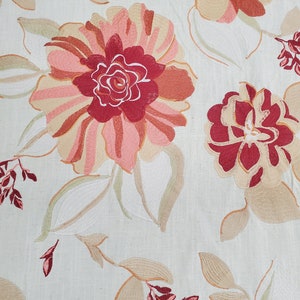 May include: A beige fabric with an embroidered floral pattern. The flowers are in shades of pink, red, and beige. The leaves are in shades of green and beige.