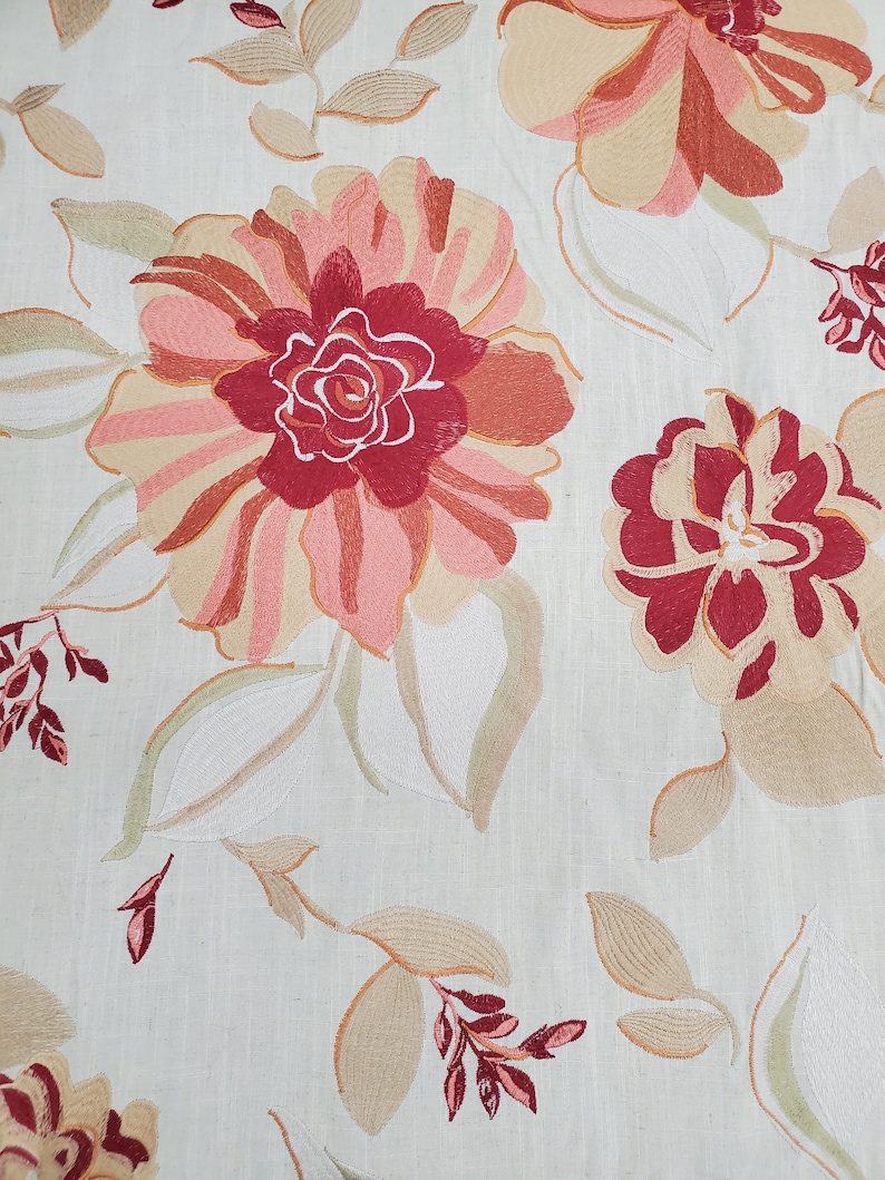 May include: A beige fabric with an embroidered floral pattern. The flowers are in shades of pink, red, and beige. The leaves are in shades of green and beige.