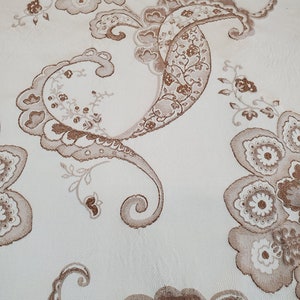 May include: A white fabric with a brown paisley pattern. The pattern features intricate floral designs and swirls.
