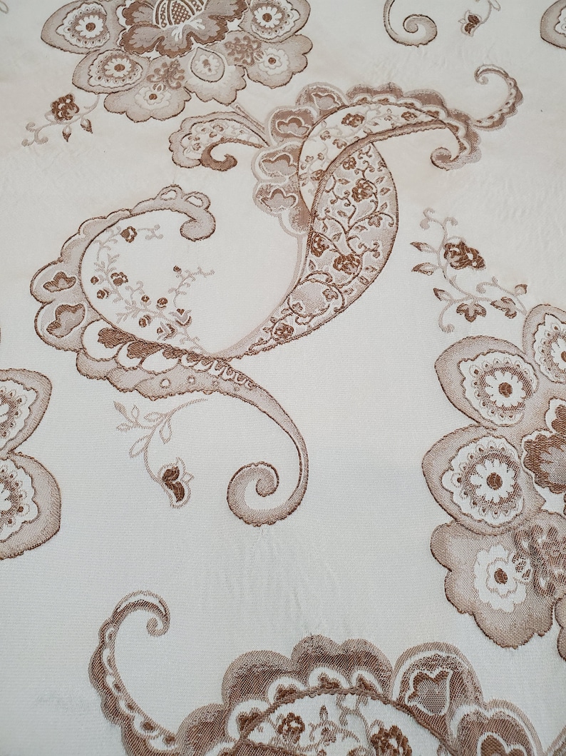 May include: A white fabric with a brown paisley pattern. The pattern features intricate floral designs and swirls.