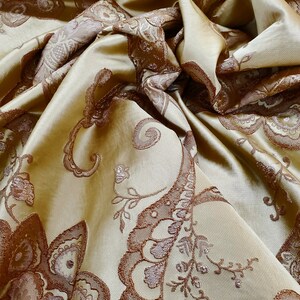 May include: A close-up of a gold fabric with a brown paisley pattern. The fabric is soft and luxurious, and the pattern is intricate and detailed.