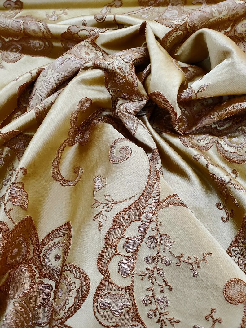 May include: A close-up of a gold fabric with a brown paisley pattern. The fabric is soft and luxurious, and the pattern is intricate and detailed.