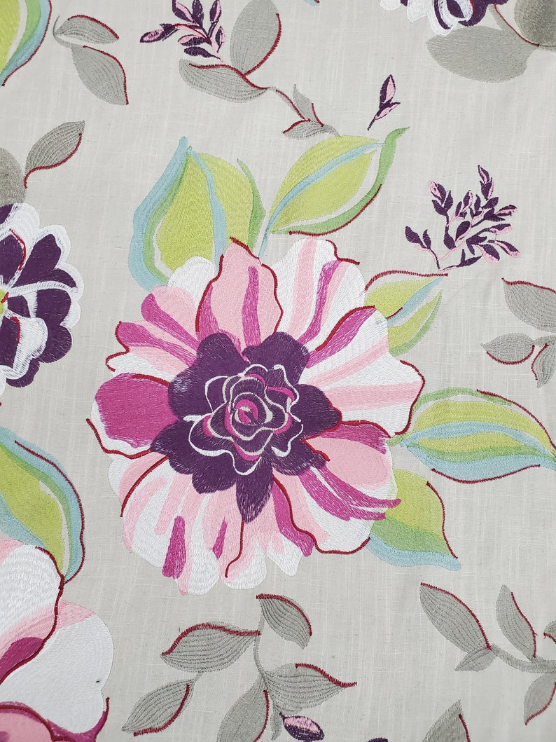 May include: A close-up of a floral fabric with a large pink and purple flower with green and blue leaves. The fabric has a light beige background.