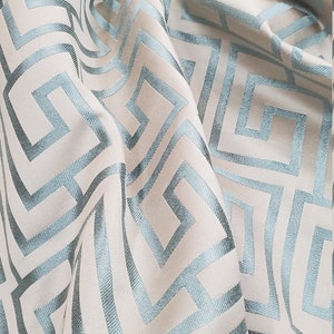 May include: A close-up of a fabric with a geometric pattern. The fabric is a light beige color with a blue geometric pattern. The pattern is made up of squares and rectangles.