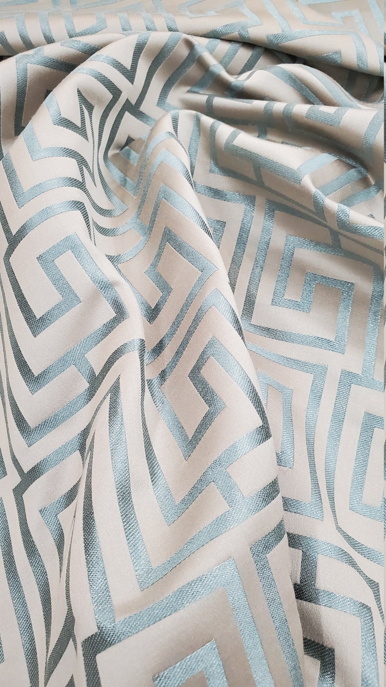 May include: A close-up of a fabric with a geometric pattern. The fabric is a light beige color with a blue geometric pattern. The pattern is made up of squares and rectangles.