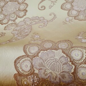 May include: Close-up of a gold fabric with a brown paisley pattern. The fabric has a subtle sheen and a soft texture.