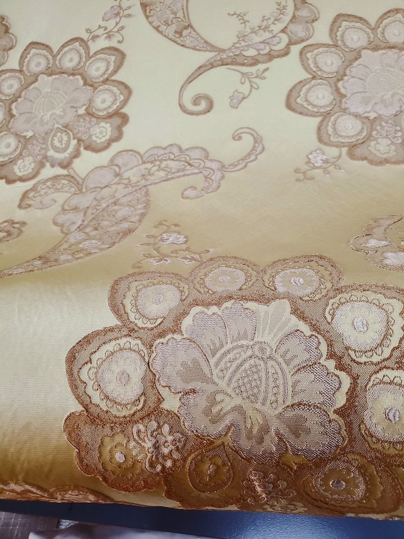 May include: Close-up of a gold fabric with a brown paisley pattern. The fabric has a subtle sheen and a soft texture.