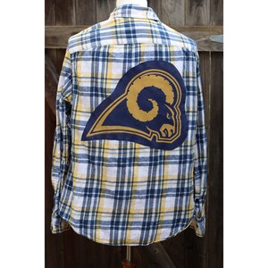 May include: A blue and yellow plaid flannel shirt with a large blue and gold Rams logo patch on the back.