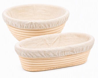 May include: Two proofing baskets for bread dough, one round and one oval, both constructed from light-colored natural cane with visible horizontal ridges and fitted with removable, off-white fabric liners that drape over the top edges.