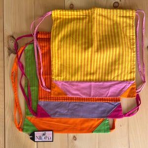 May include: Four colorful drawstring bags stacked on top of each other. The top bag is yellow and orange with pink trim. The second bag is orange and green with pink trim. The third bag is purple and orange with pink trim. The bottom bag is orange and green with pink trim. The bags have a label that says "Niliptha".
