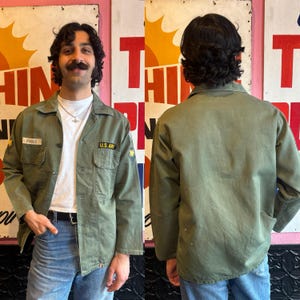 Könnte beinhalten: Eine grüne Jacke im Militärstil mit einem Aufnäher, auf dem "U.S. Army" steht, und einem weiteren Aufnäher, auf dem "FOGGE" steht.