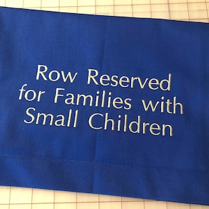 May include: A blue fabric sign with white embroidery that reads "Row Reserved for Families with Small Children".