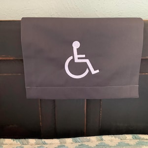 May include: A gray fabric headboard with a white wheelchair accessibility symbol embroidered on it.