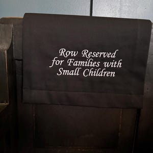 May include: A black fabric sign with white text that reads "Row Reserved for Families with Small Children".