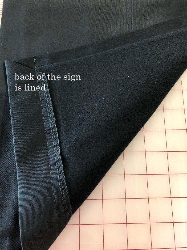 May include: Close-up of a black fabric with a lined interior. The text "back of the sign is lined" is visible. The fabric is folded, revealing the interior lining and the stitching along the edge.