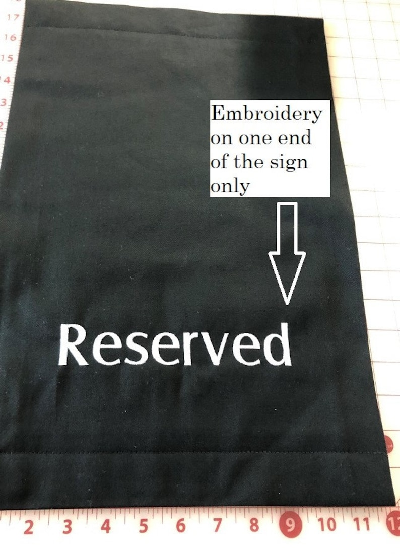 May include: Black fabric sign with the word "Reserved" embroidered in white. The sign has a simple design, with the text prominently displayed. The image also includes the text "Embroidery on one end of the sign only".