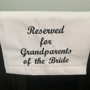 May include: White fabric sign with black embroidered text that reads "Reserved for Grandparents of the Bride".