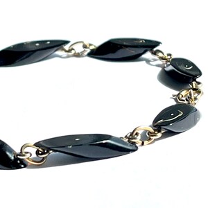 May include: A vintage bracelet featuring black, teardrop-shaped beads linked by gold-tone metal chain. The beads have a glossy finish, and the chain has a delicate design. The bracelet is set against a white background.