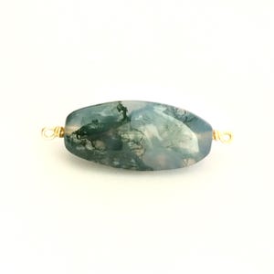 May include: A green moss agate bead with gold-toned wire loops on either end. The bead is oval-shaped and has a mottled green and white pattern.