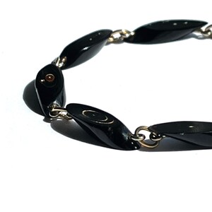 May include: A black beaded bracelet with oval-shaped beads connected by silver-colored chain links. The beads have a glossy finish and are evenly spaced. The bracelet is set against a white background.
