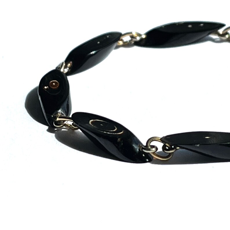 May include: A black beaded bracelet with oval-shaped beads connected by silver-colored chain links. The beads have a glossy finish and are evenly spaced. The bracelet is set against a white background.