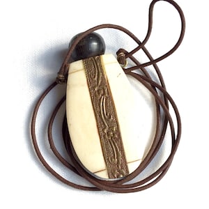 May include: A white oval pendant with a gold floral design and a brown leather cord. The pendant has a dark wood top.