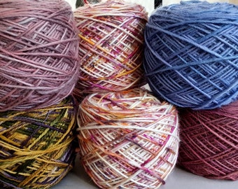 May include: A collection of six yarn skeins in various colors. The skeins are tightly wound and display a mix of hues, including shades of purple, blue, yellow, and white. The yarn appears to be a natural fiber, suitable for knitting or crochet projects.