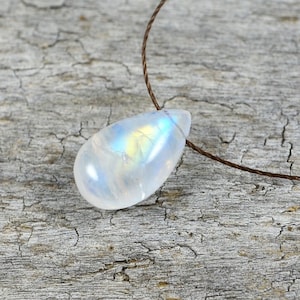May include: A teardrop-shaped moonstone pendant on a brown cord necklace. The moonstone is iridescent with a rainbow of colors.