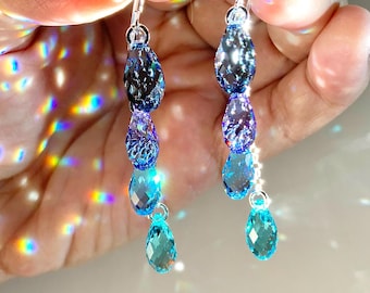 Puede incluir: Pendientes colgantes con una serie de cristales azules en forma de lágrima. Los pendientes tienen un degradado de colores, desde el azul oscuro hasta el turquesa claro. Los cristales cuelgan de ganchos plateados.