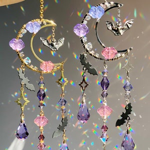 May include: Two crystal suncatchers with a crescent moon design, featuring purple and pink beads, bat charms, and a crystal prism at the bottom.