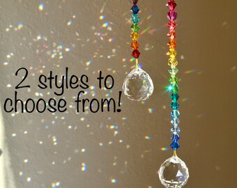 Puede incluir: Dos atrapasoles de cristal con cuentas de colores arcoíris que cuelgan de cadenas doradas. Los atrapasoles tienen bolas de cristal transparentes en la parte inferior. El texto "2 styles to choose from!" es visible en la imagen.
